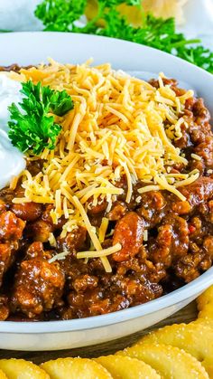 a bowl filled with chili and cheese next to crackers