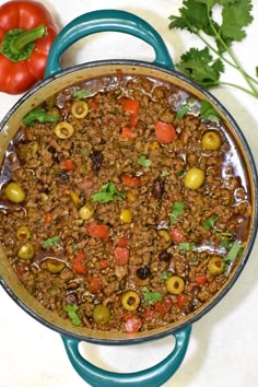 a pot filled with meat and olives on top of a white counter next to tomatoes