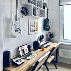 a laptop computer sitting on top of a wooden desk next to a guitar hanging from the wall