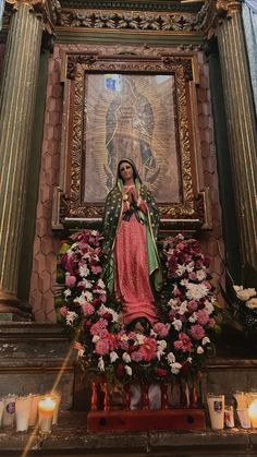 the virgin mary statue is surrounded by flowers and candles in front of an ornate painting