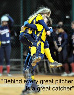 two softball players in blue and yellow uniforms hugging each other on a baseball field with the words behind every great pitcher is a great catcher