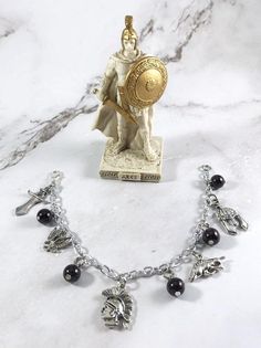 a silver bracelet with black beads and a statue on the top, sitting on a marble surface