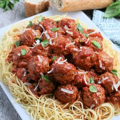 spaghetti and meatballs with parmesan cheese are on a white plate next to bread