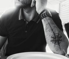 a man sitting at a table talking on a cell phone with a compass tattoo on his arm