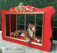 a fake tiger in a cage on the ground next to a wall with green plants