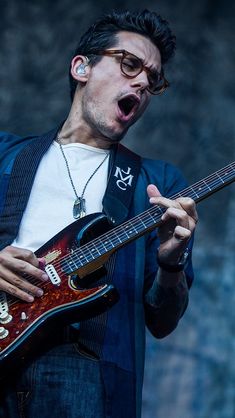 a man holding a guitar and making a face with his mouth wide open while wearing glasses