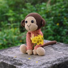 a crocheted monkey sitting on top of a rock with flowers in it's lap