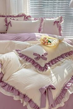 a bed with purple ruffles and pillows on it in front of a window