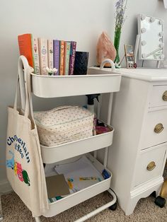 a white desk with books and a bag on it next to a dresser in a bedroom