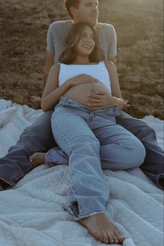 a pregnant woman sitting on top of a man laying on the ground next to her