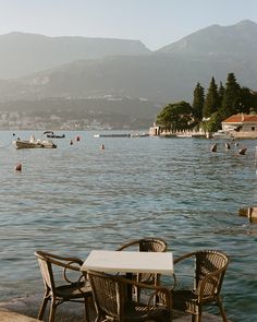 two chairs and a table sitting on the edge of a body of water