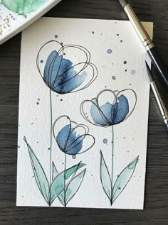 a watercolor painting of blue flowers on white paper next to a pen and brush