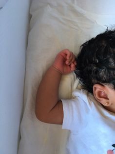 a small child laying on top of a bed next to a white sheet and pillow