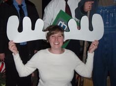 a woman in white shirt holding up two fake moose antlers over her head while standing next to other people