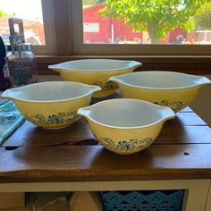 four yellow and white bowls sitting on top of a wooden table next to a window