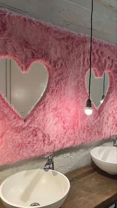 two sinks are in front of a pink wall with heart shaped mirrors on the side