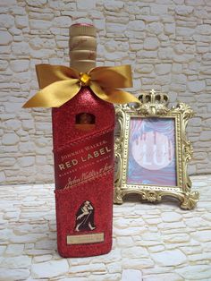 a red wine bottle with a gold bow on it next to a picture frame and wall