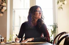 a woman sitting at a desk writing on a piece of paper with a pen in her hand