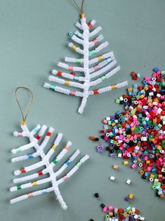 two christmas tree ornaments made out of plastic beads and colored sprinkles on a gray surface