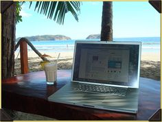 an open laptop computer sitting on top of a wooden table next to a glass of drink