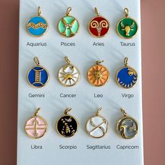 twelve zodiac signs in different colors on a white sheet with gold accents and charms attached to them