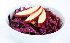 a white bowl filled with red cabbage and apples