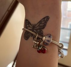 a close up of a person's arm with a butterfly and charms on it