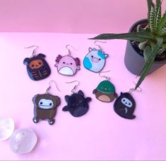 six different animal shaped earrings sitting next to a potted plant on a pink surface