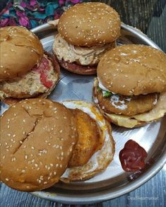 four hamburgers on a metal plate with ketchup