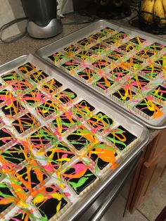 two trays filled with decorated cookies sitting on top of a counter next to bananas