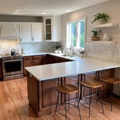 a large kitchen with wooden floors and white counter tops, two stools at the island