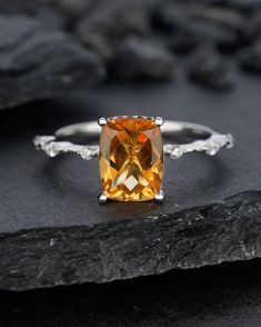 an orange and white diamond ring sitting on top of a black stone slab with rocks in the background