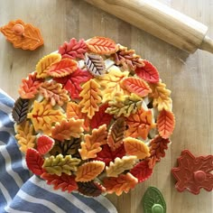 a wooden cutting board topped with lots of colorful fall leaves next to cookie cutters