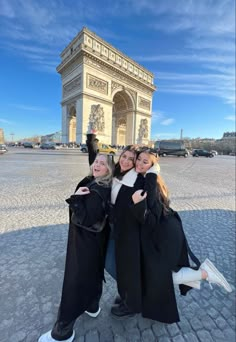 three women in black coats posing for a photo at the arc de trioe triumph