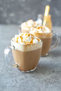 two mugs filled with hot chocolate and whipped cream on a gray countertop next to each other