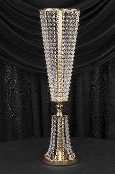 a golden vase with crystal beads on it's sides and a black curtain in the background