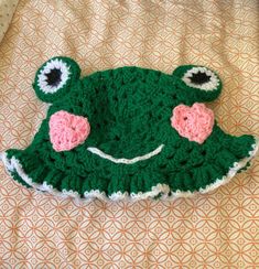 a green crocheted hat with pink flowers on it sitting on top of a bed