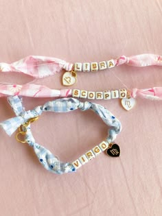 three bracelets with name charms on them sitting on a pink cloth covered tablecloth