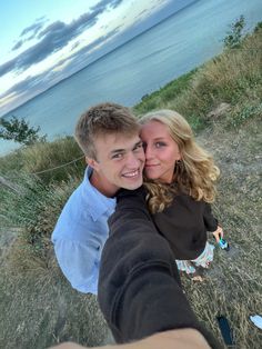 a man and woman taking a selfie with the ocean in the backgroud