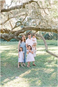 a family posing for a photo under a large tree in the grass with spanish moss