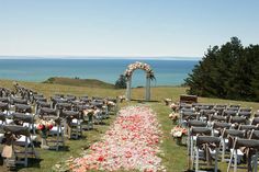 an outdoor ceremony set up with chairs and flowers on the aisle, overlooking the ocean