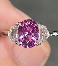 a close up of a person holding a ring with a pink stone in it's center