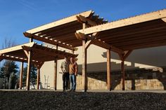 two people standing in front of a building with wooden beams on the roof and walls