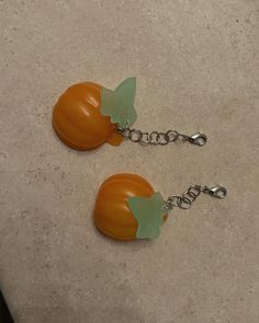 two oranges with green leaves on them are hanging from silver chain earring hooks