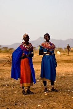 two women in traditional african clothing standing on the ground with their arms around each other