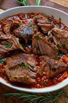 meat stew in a white bowl on a wooden table with herbs and spices around it