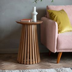 a pink chair next to a table with a vase on it and a yellow pillow