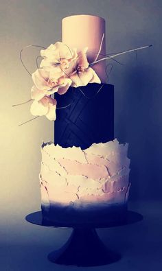 a three tiered cake with white and black frosting, flowers on the top