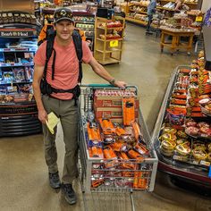 a man standing next to a shopping cart in a store filled with food and snacks