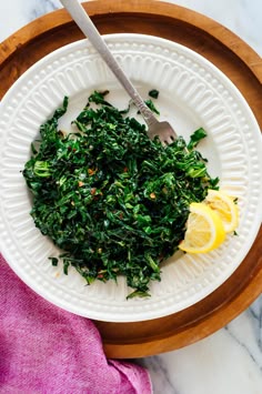 a white plate topped with greens and lemon wedges next to a pink napkin on top of a marble counter